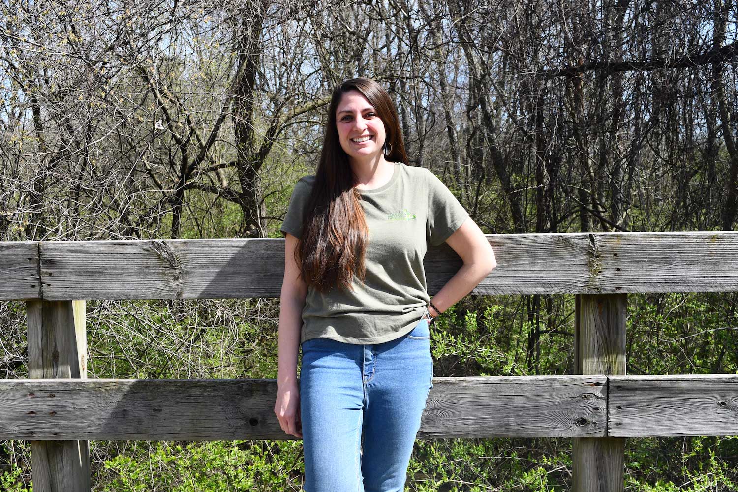 A person standing against a wooden fence with trees in the background.