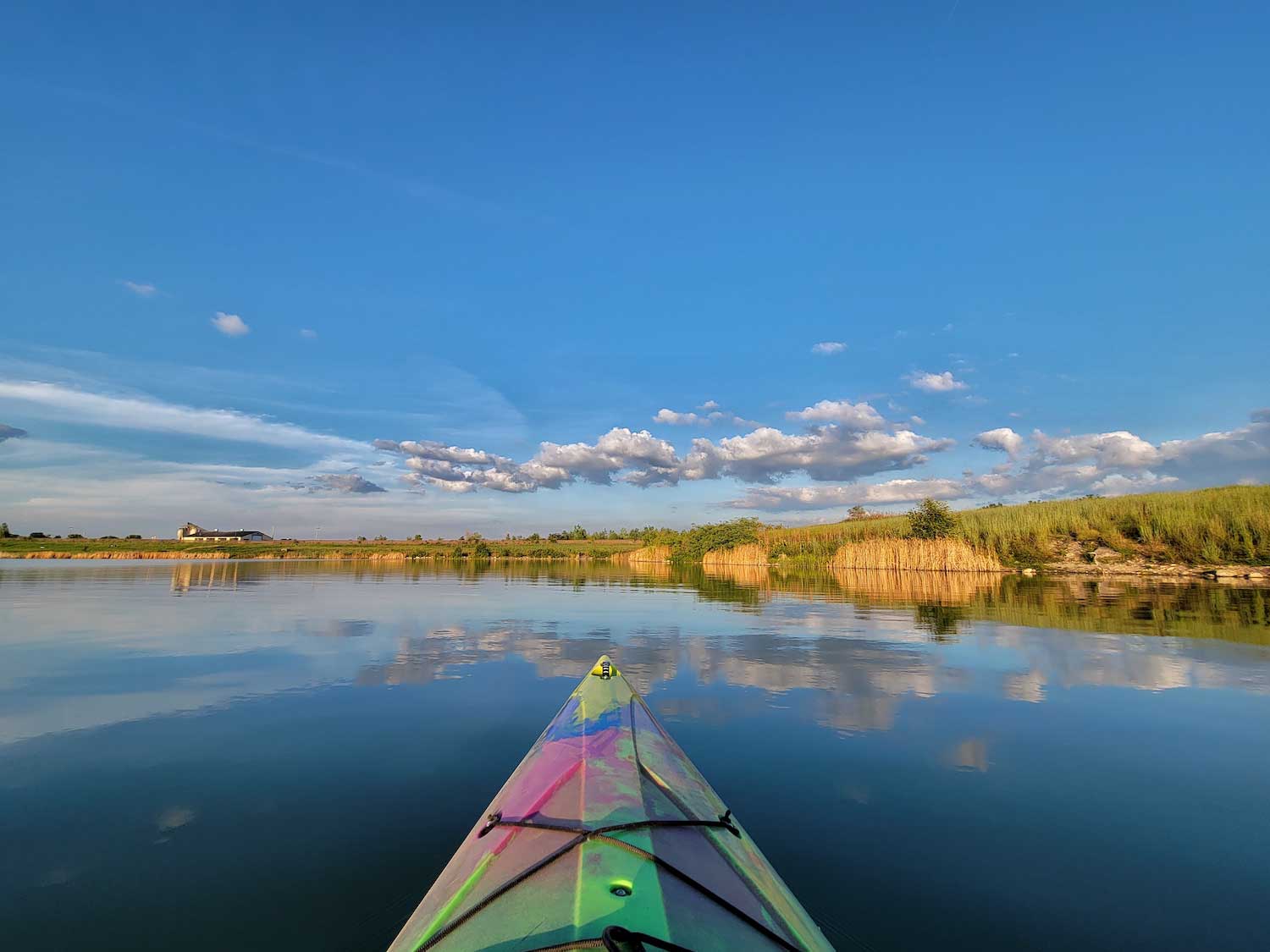 The front of a kayak on open water with a blue sky above.