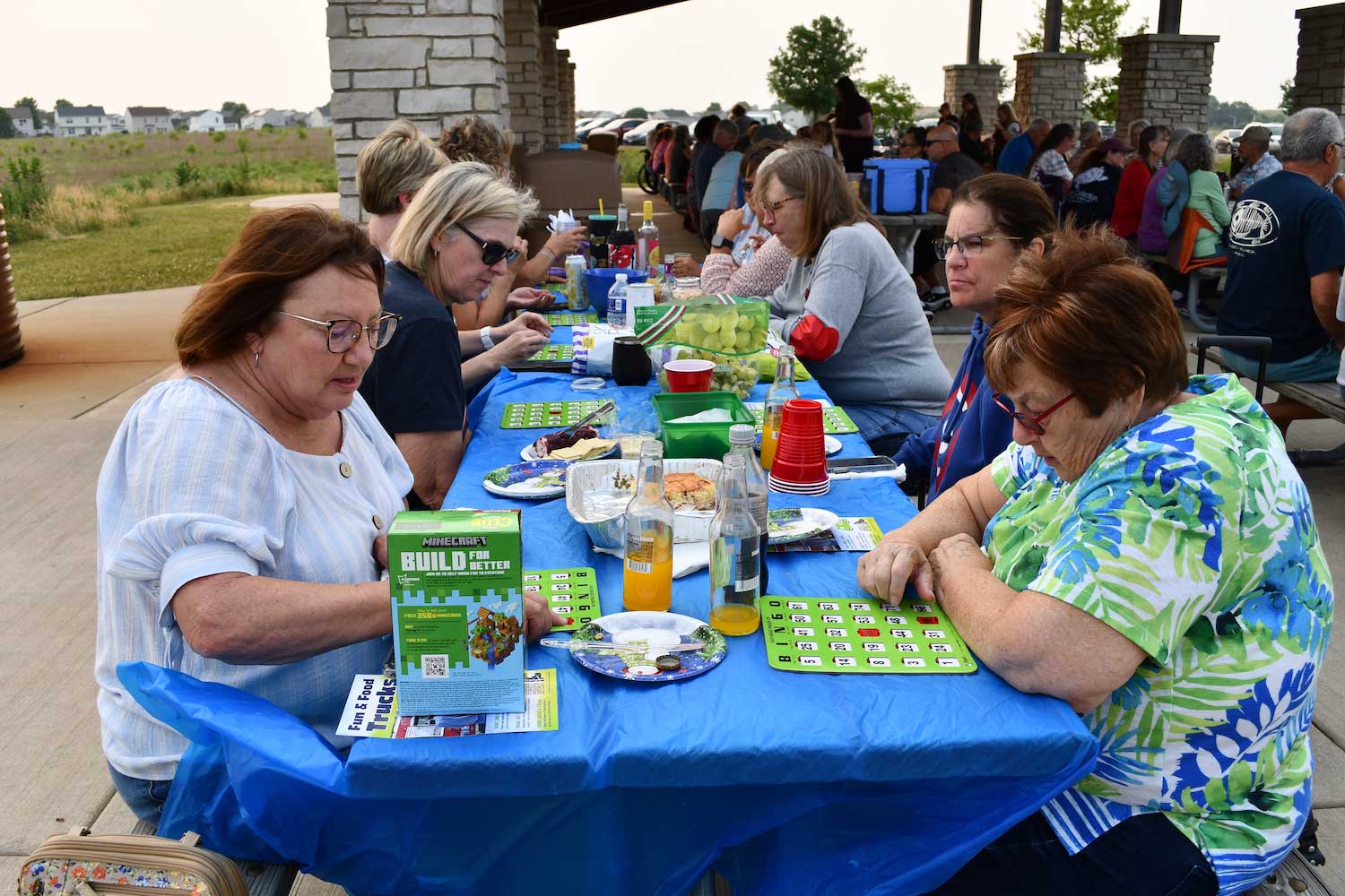 People sitting at picnic tables playing bingo outside.