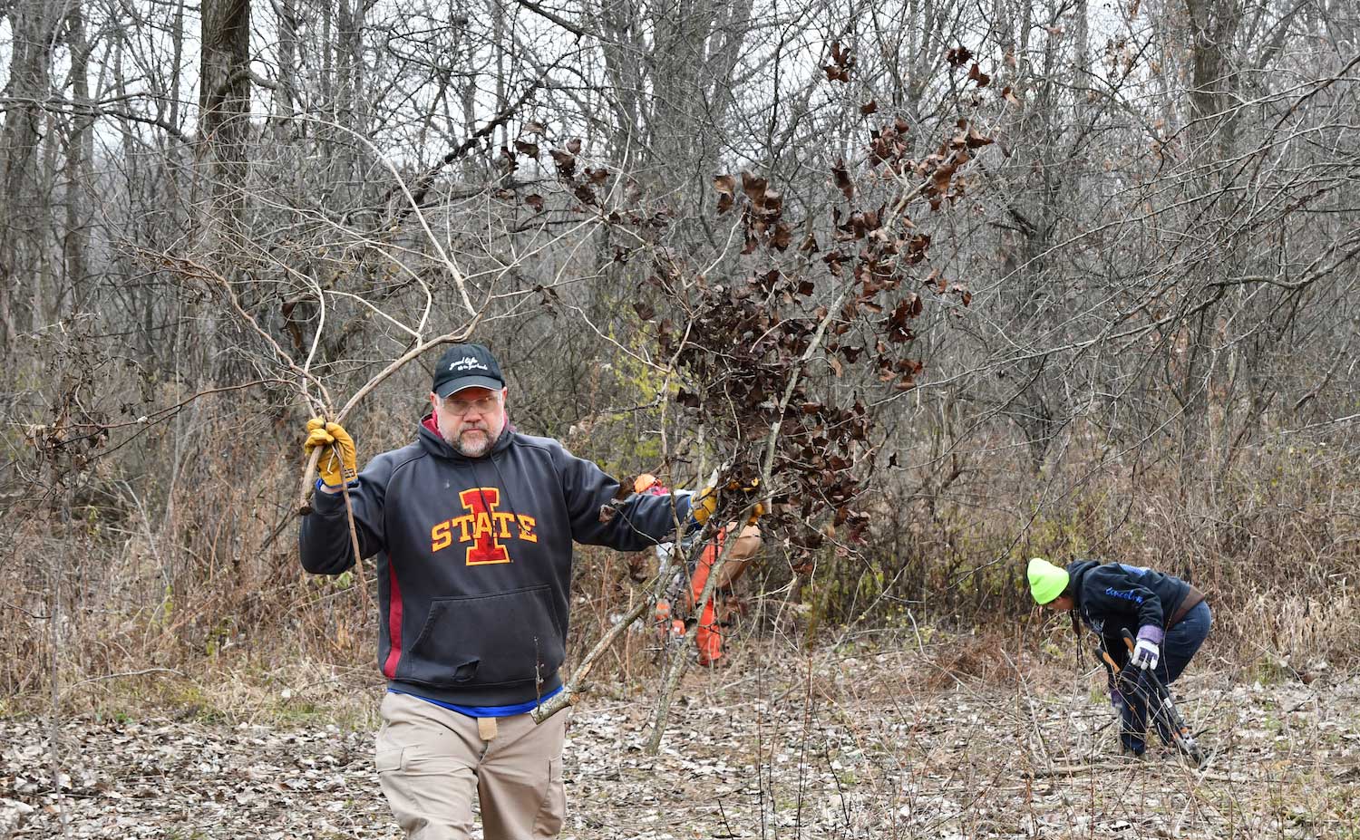 A person walking through a natural area carrying sticks in both hands.