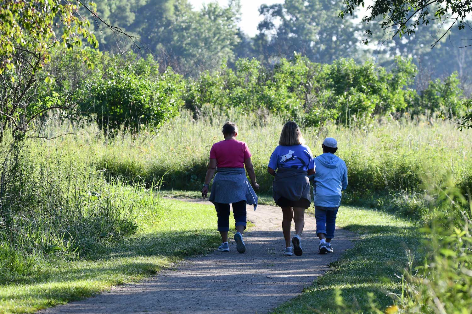 Three people walking side by side together on a trail seen from behind.