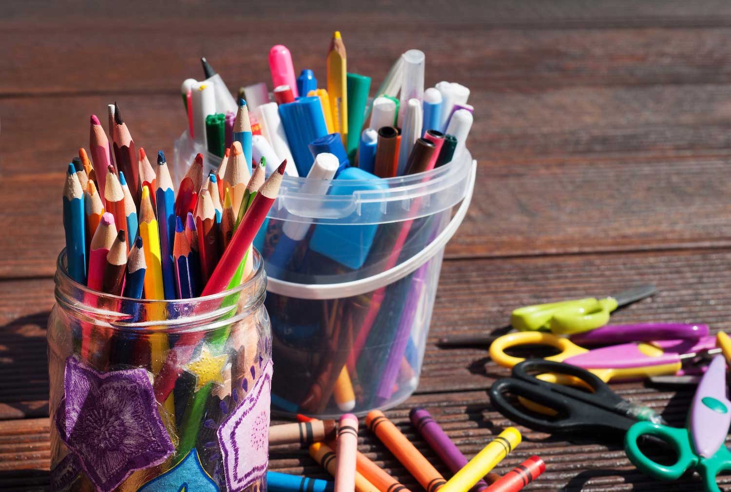 Containers of markers, colored pencils and crayons on a wooden table.