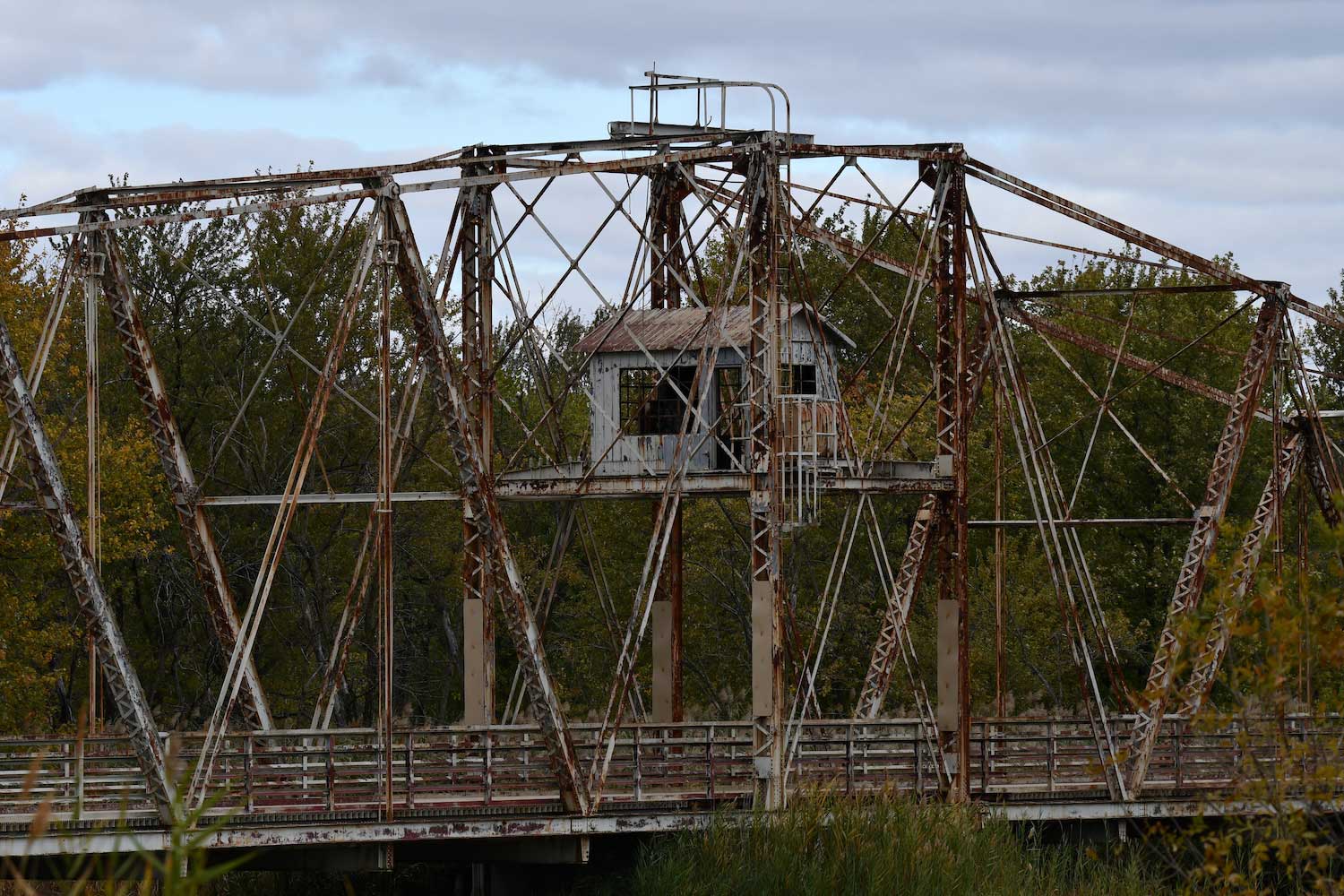 A rusted old swing bridge surrounded by trees and grasses.