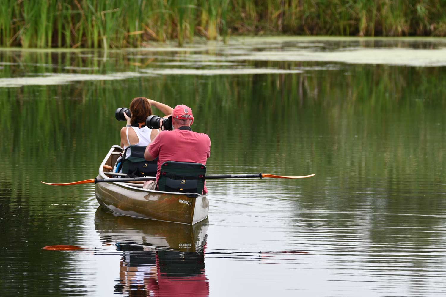 Two people taking photos with cameras while on a canoe on the water.