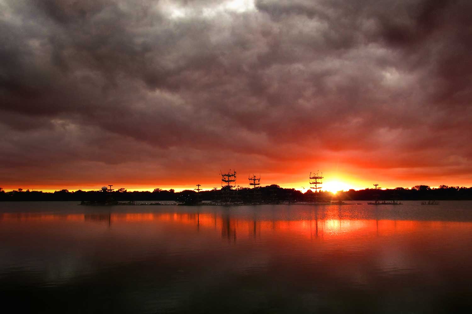 An orange and red sky as the sun sets behind a lake with nesting platforms visible in the distance.