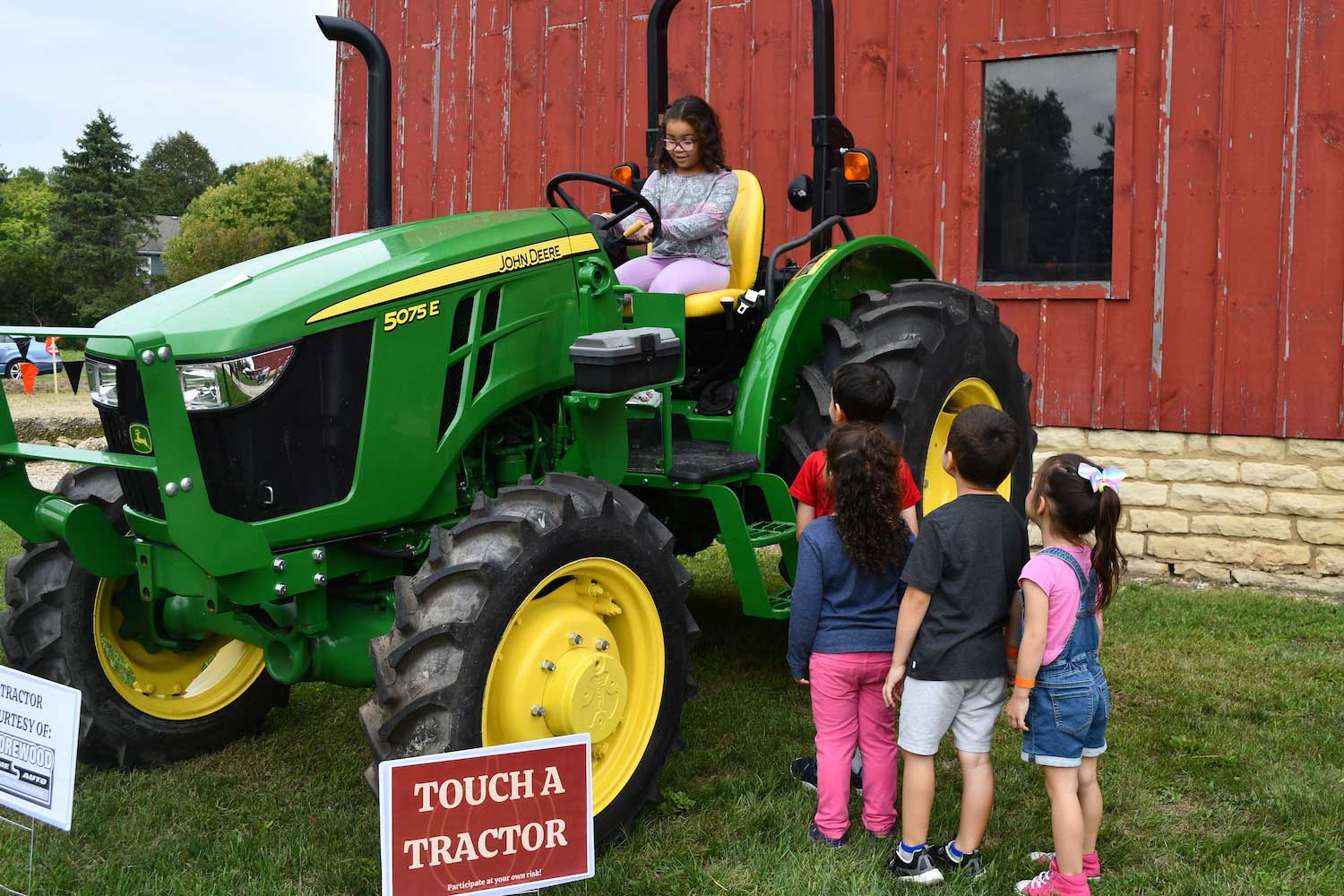 A child sitting on a green John Deere tractor while a line of kids waits for their turns.
