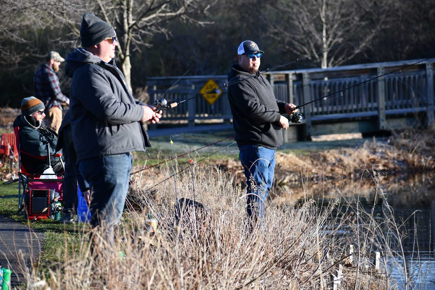 Two people standing along a shoreline fishing with sitting in the background. 