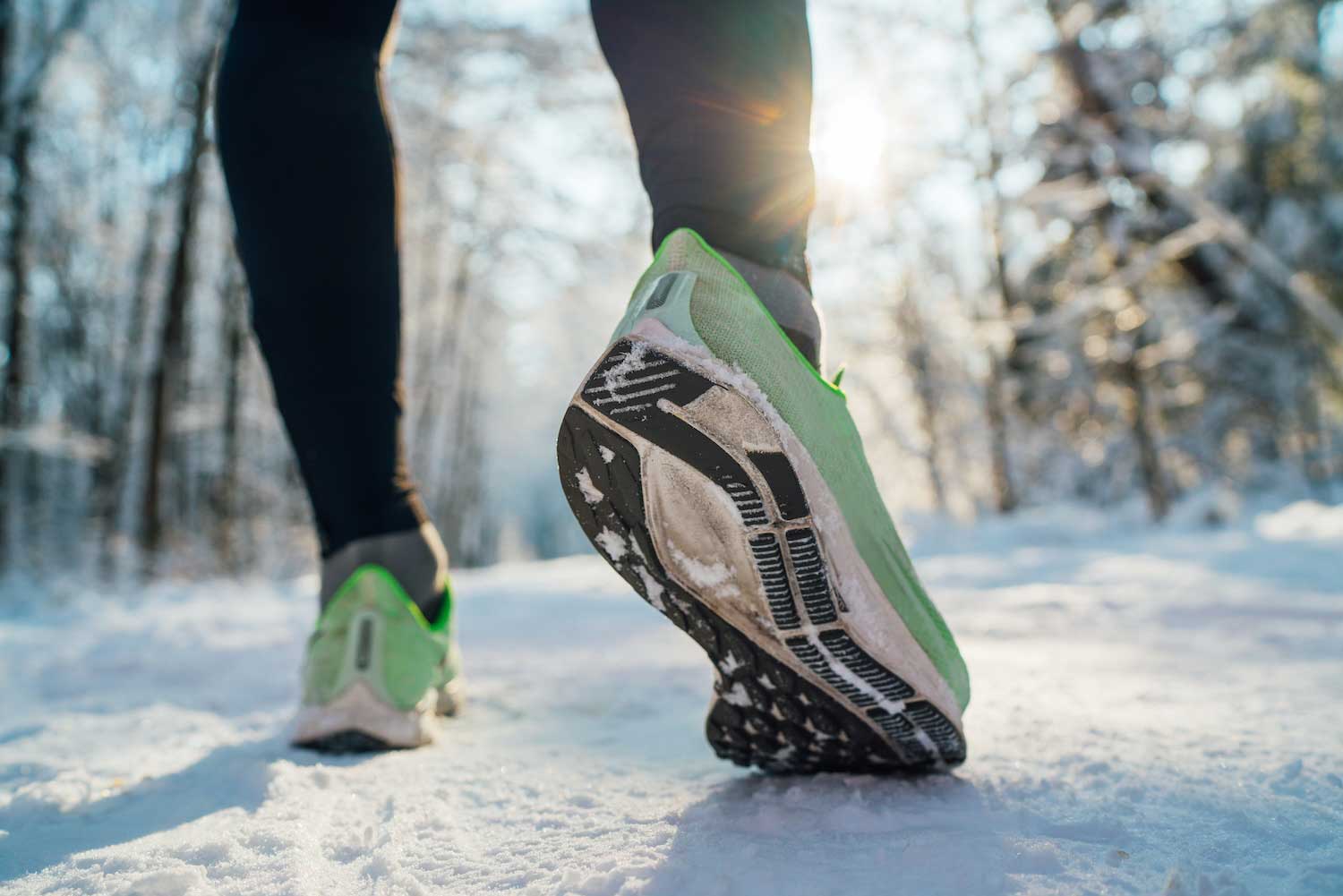 A closeup of feet in running shoes on a snow-covered trail.