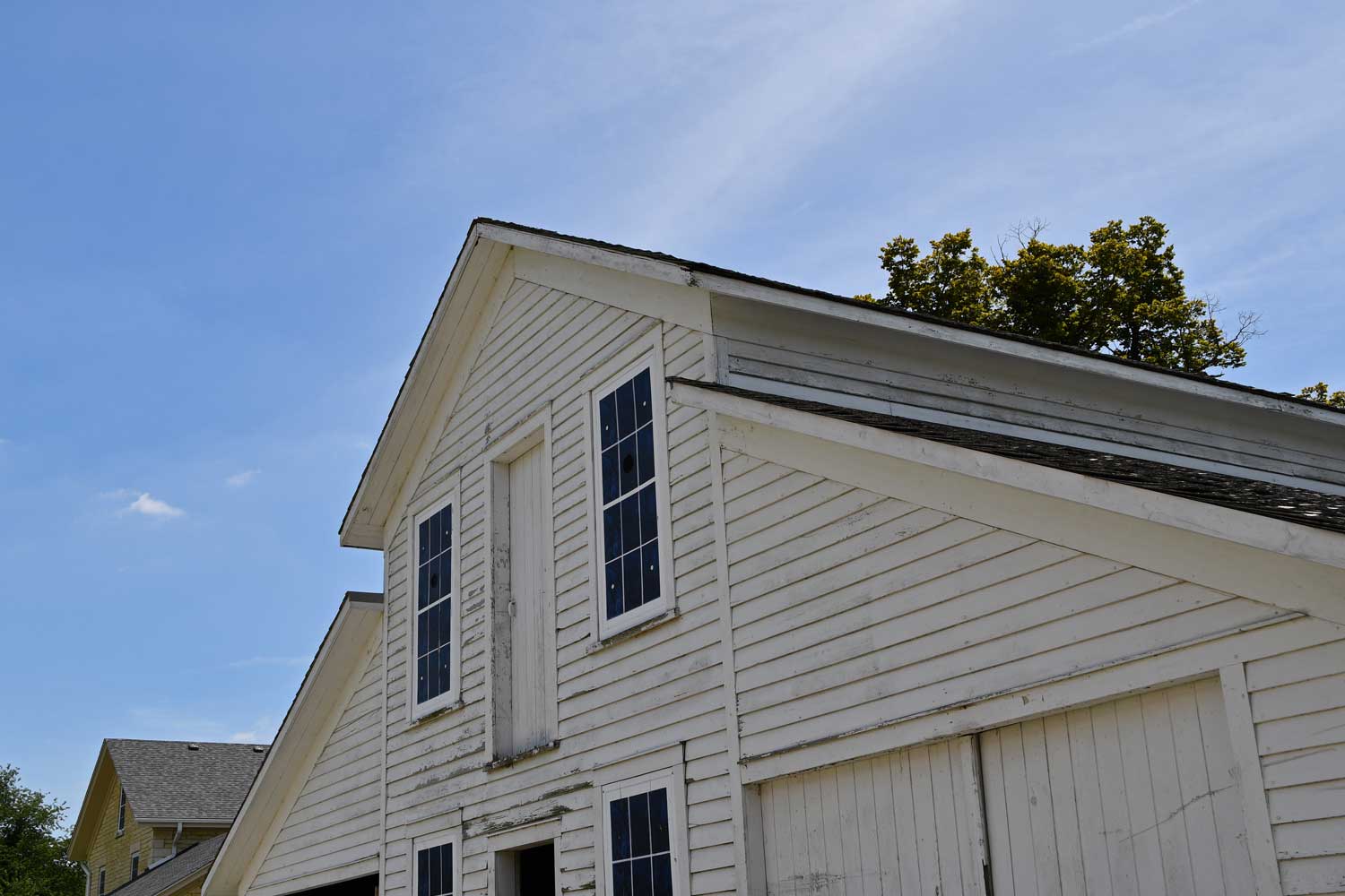 The top story of an old white farmhouse with the blue sky as a backdrop.