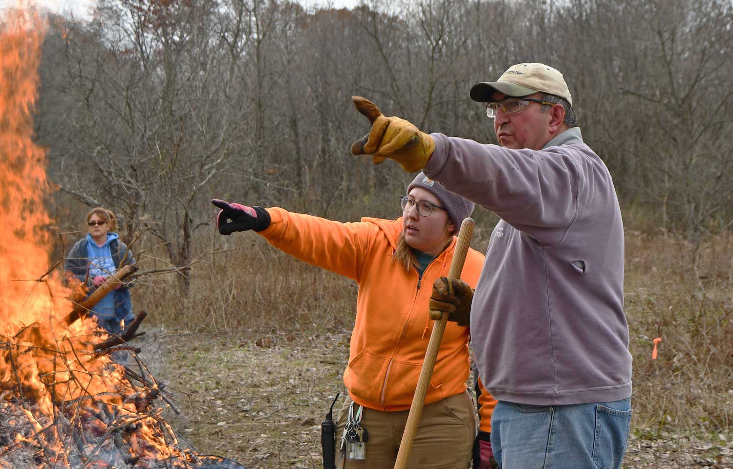 Two people pointing to the left while standing next to a brush pile.