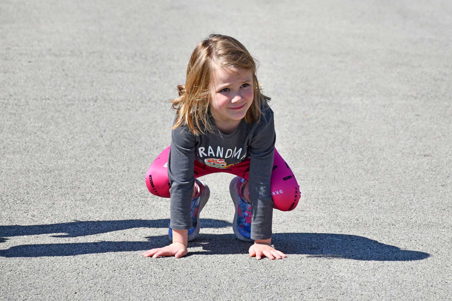A child crouched down on the pavement ready to leap.