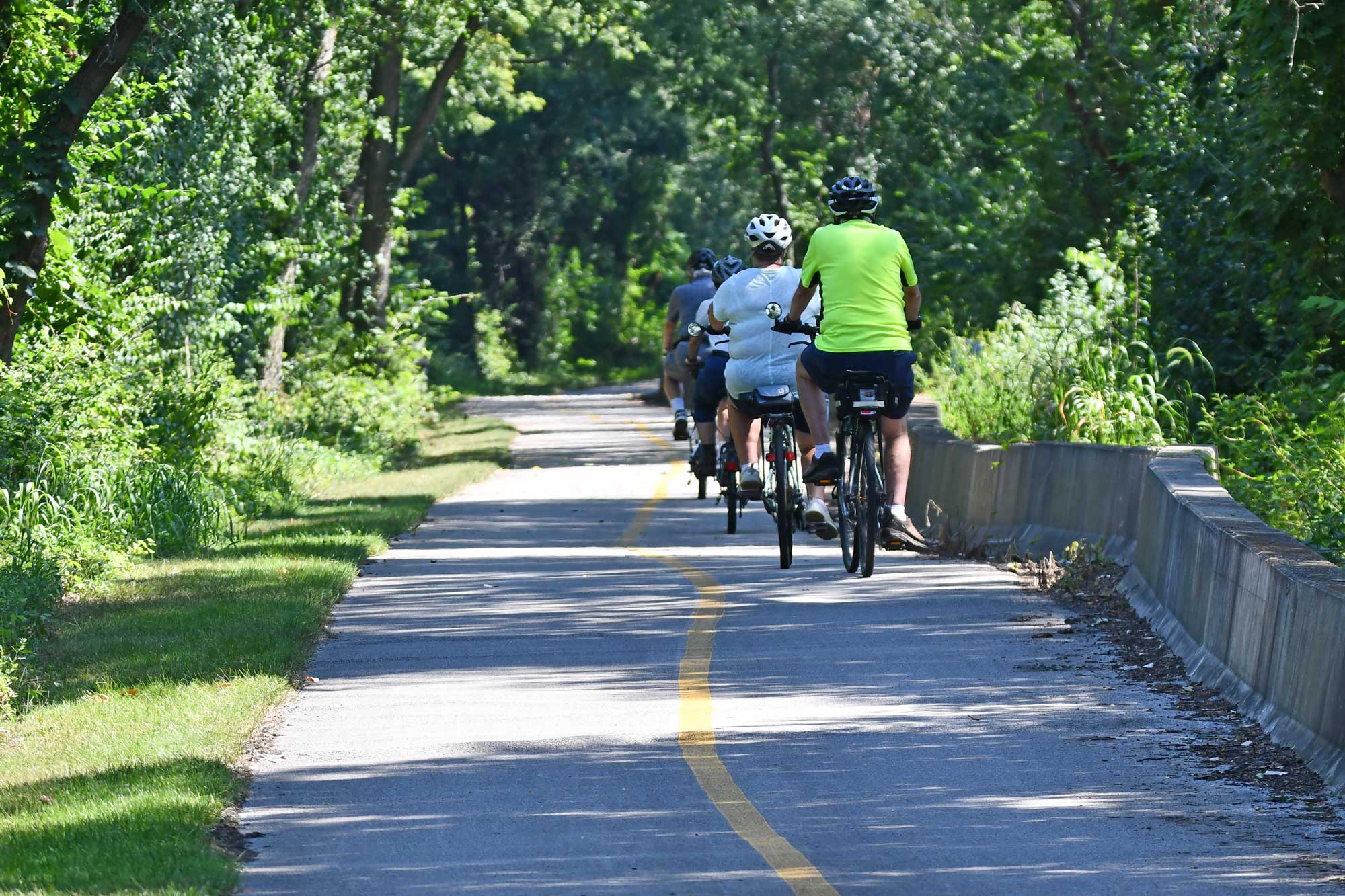 Bikers ride along a paved trail.