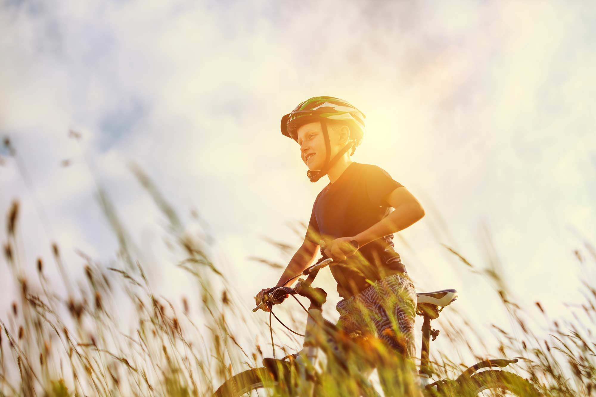 A child wearing a bike helmet while riding a bike on a trail with tall prairie grasses in the background.