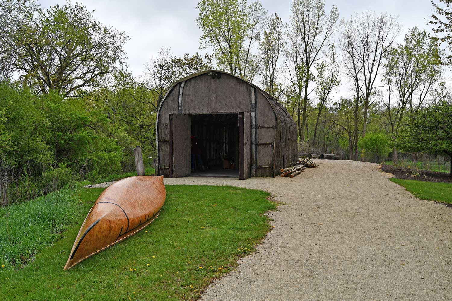 The exterior of a Native American longhouse with a canoe on the ground outside.