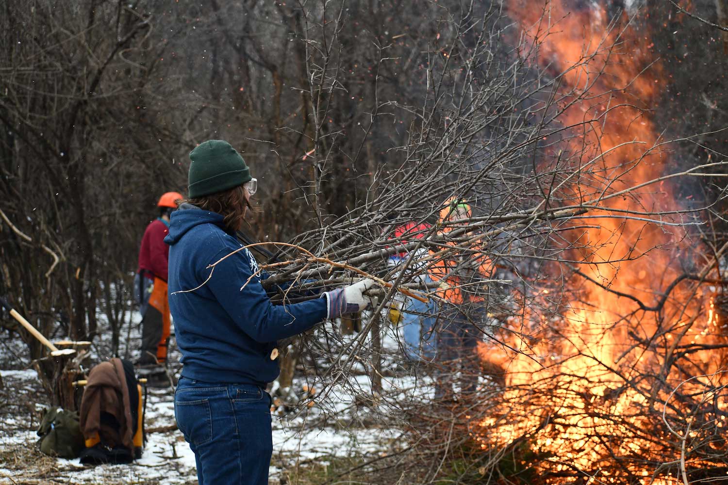 A person adding branches to a burning brush pile.