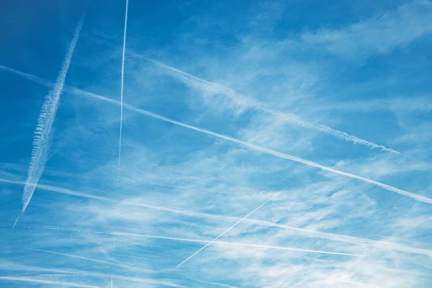 Contrails criss-crossing the sky with thin, scattered clouds above them.
