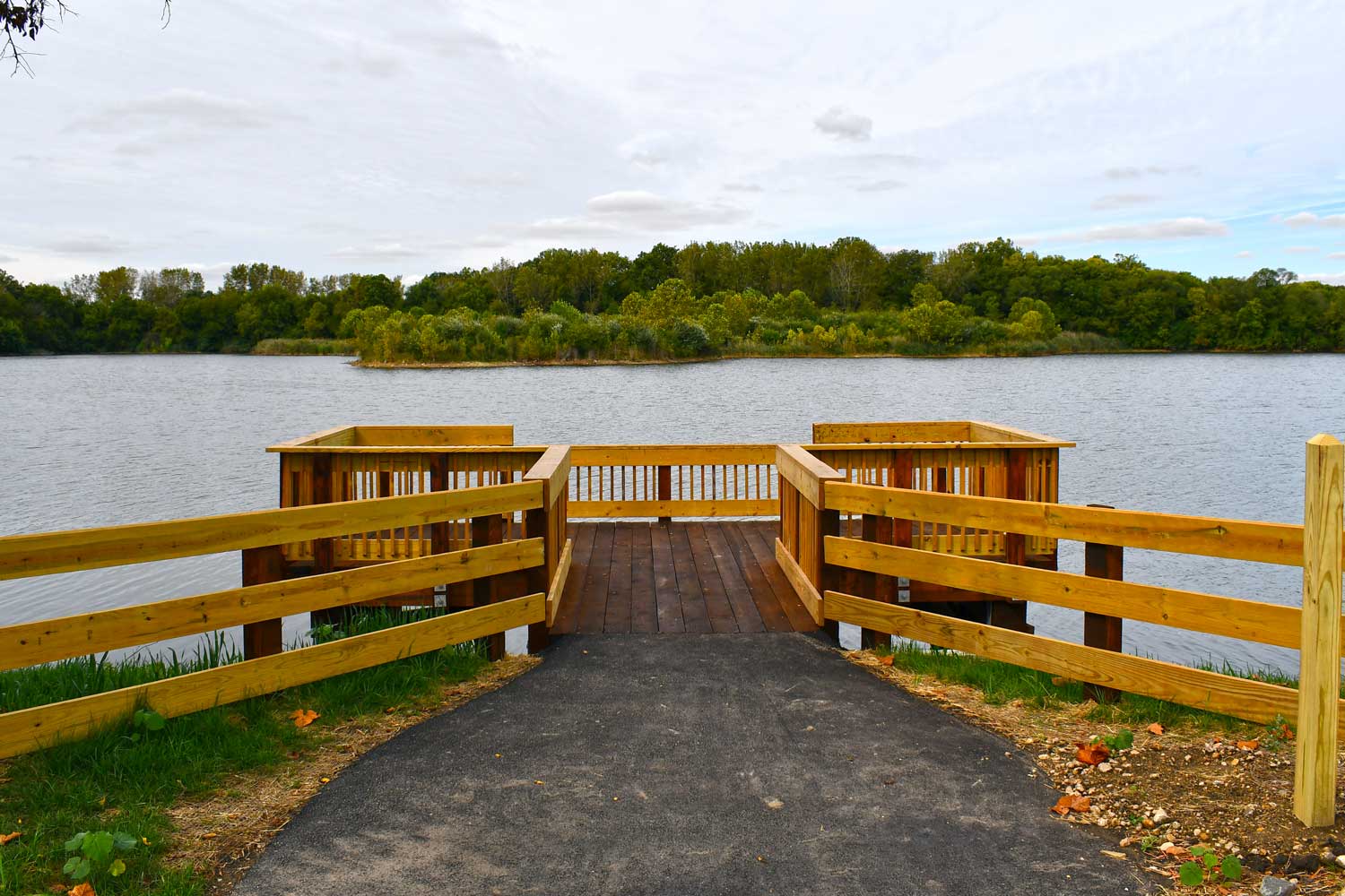 Fishing pier overlooking a lake with trees in the background.