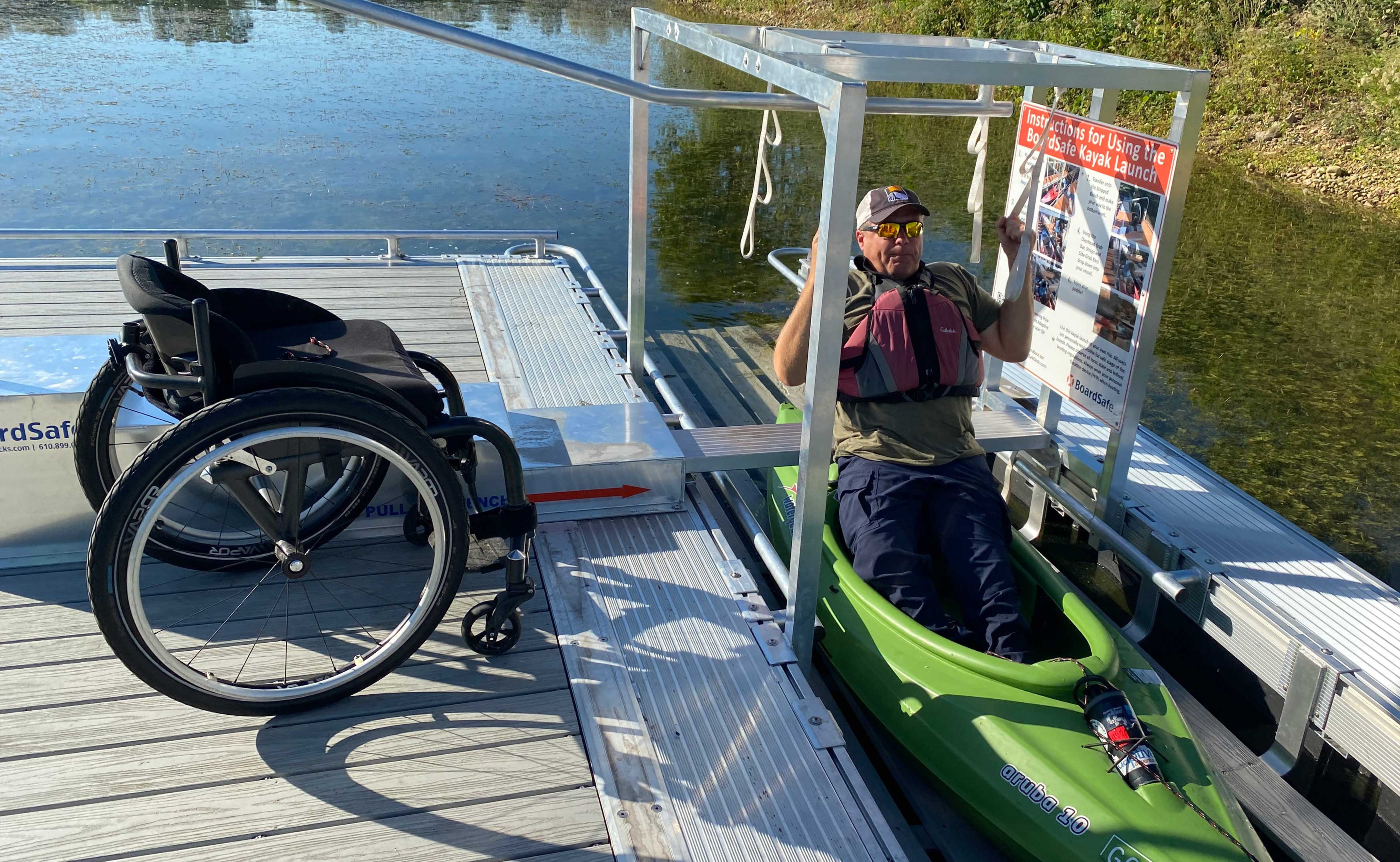 A man gets out of his wheelchair and into a kayak in an accessible kayak launch