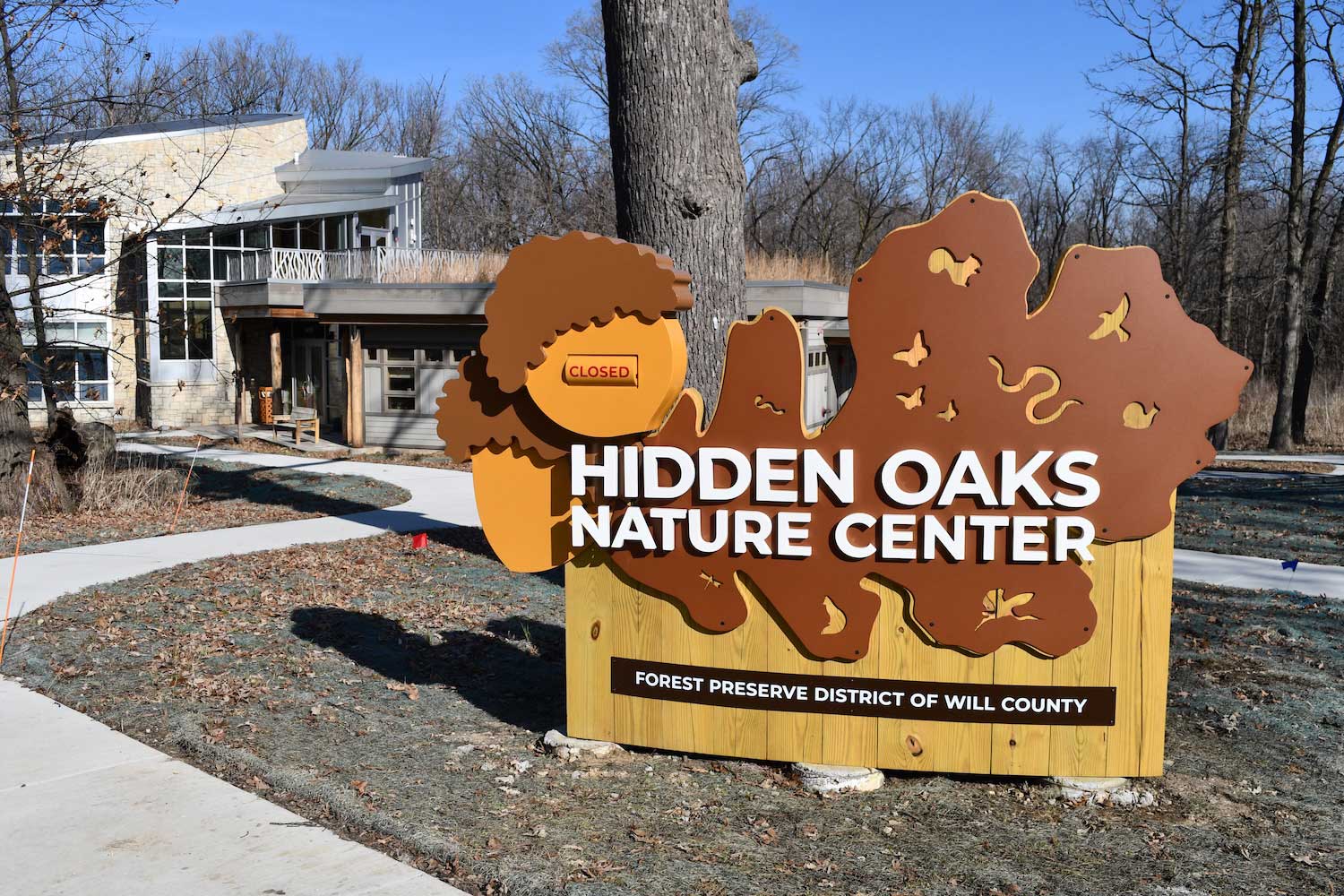 A wooden and metal sign for Hidden Oaks Nature Center outside a building.