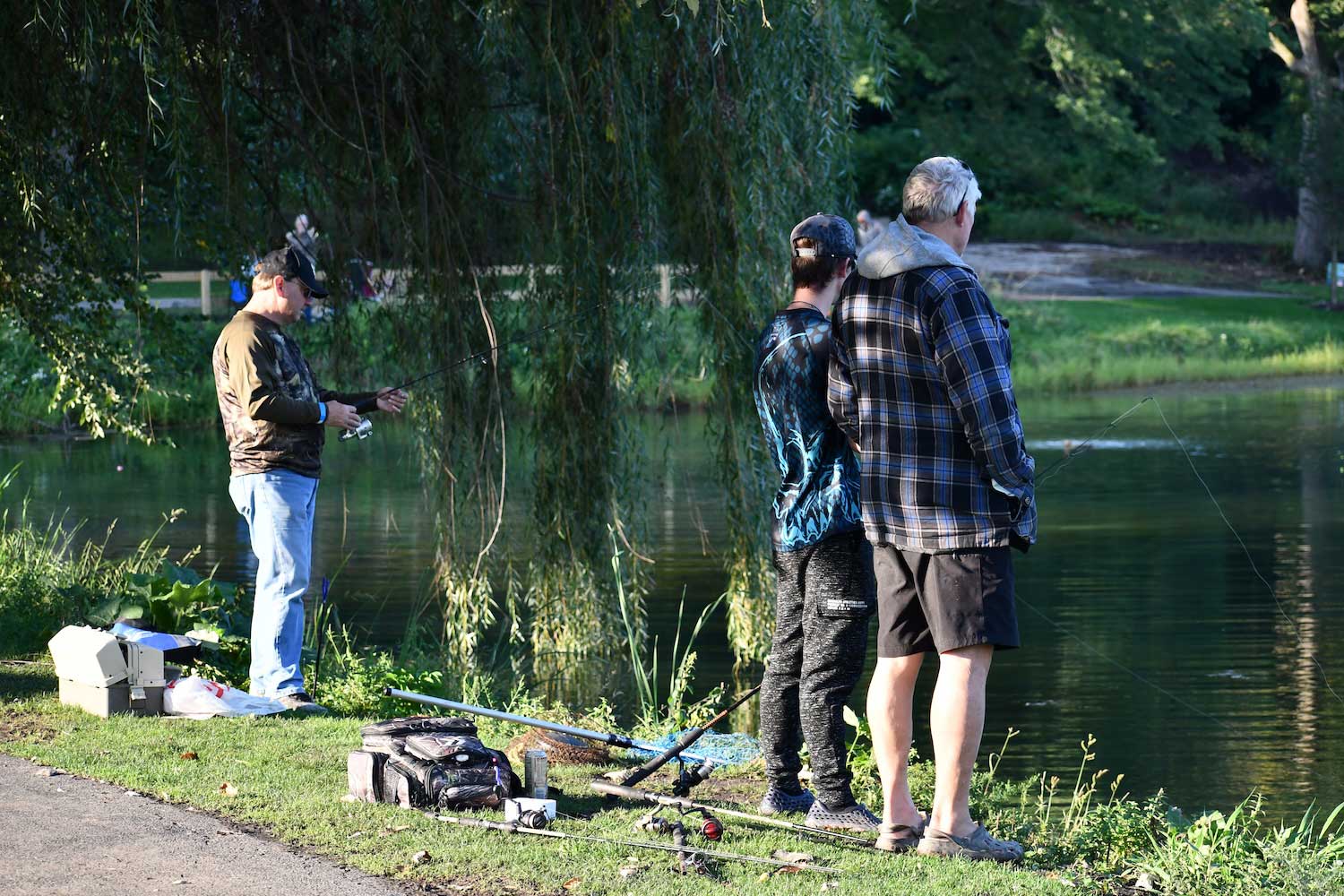 Three people fishing along the shore of a small lake.