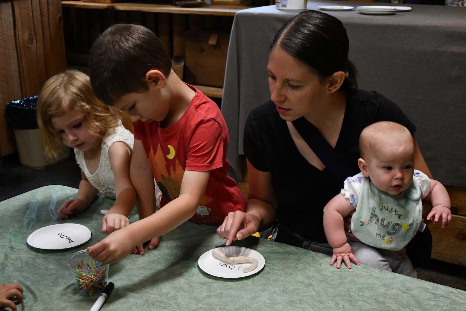 An adult and three young kids working on a craft at a table.