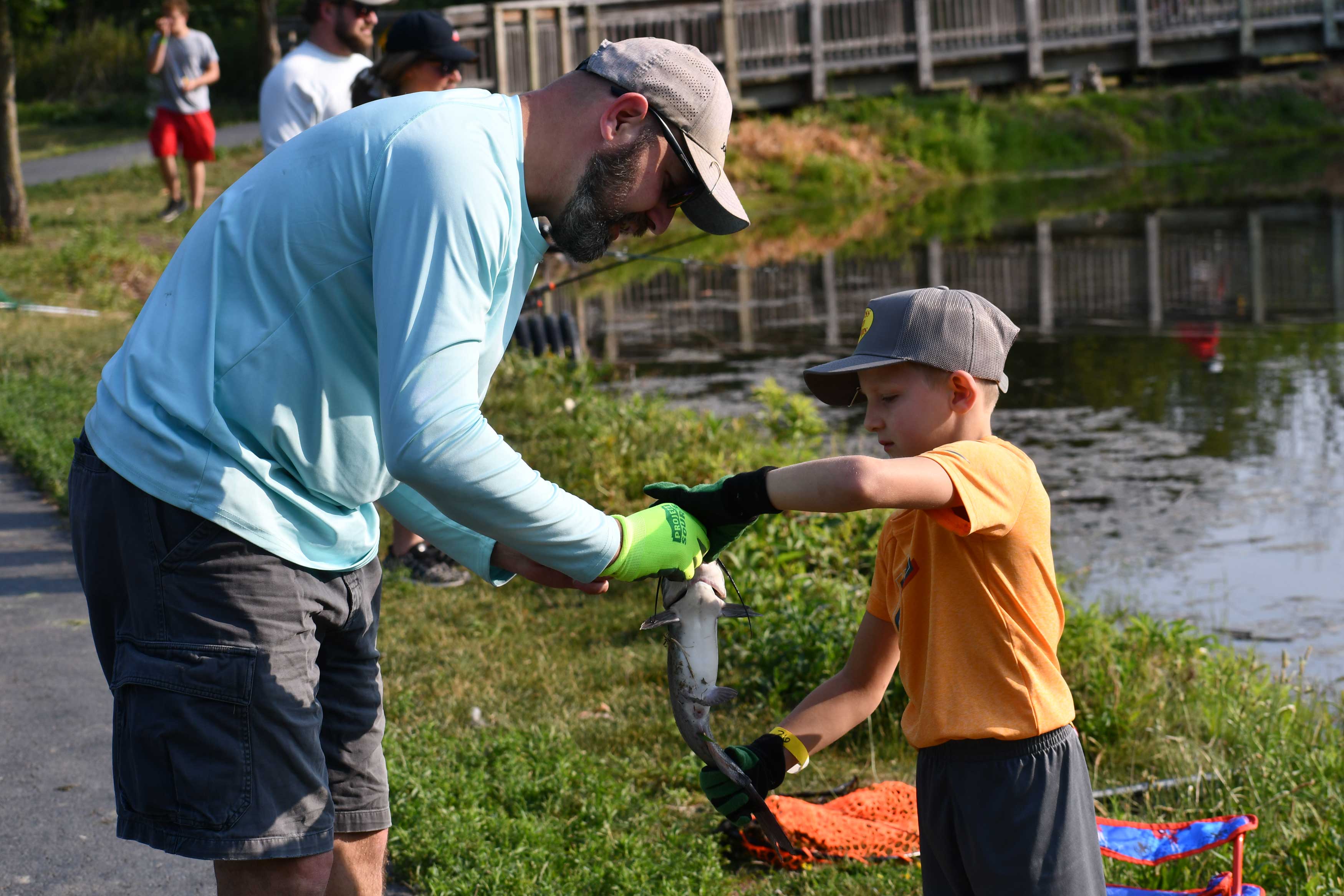 A man helps a young boy with a fish on the end of a line.