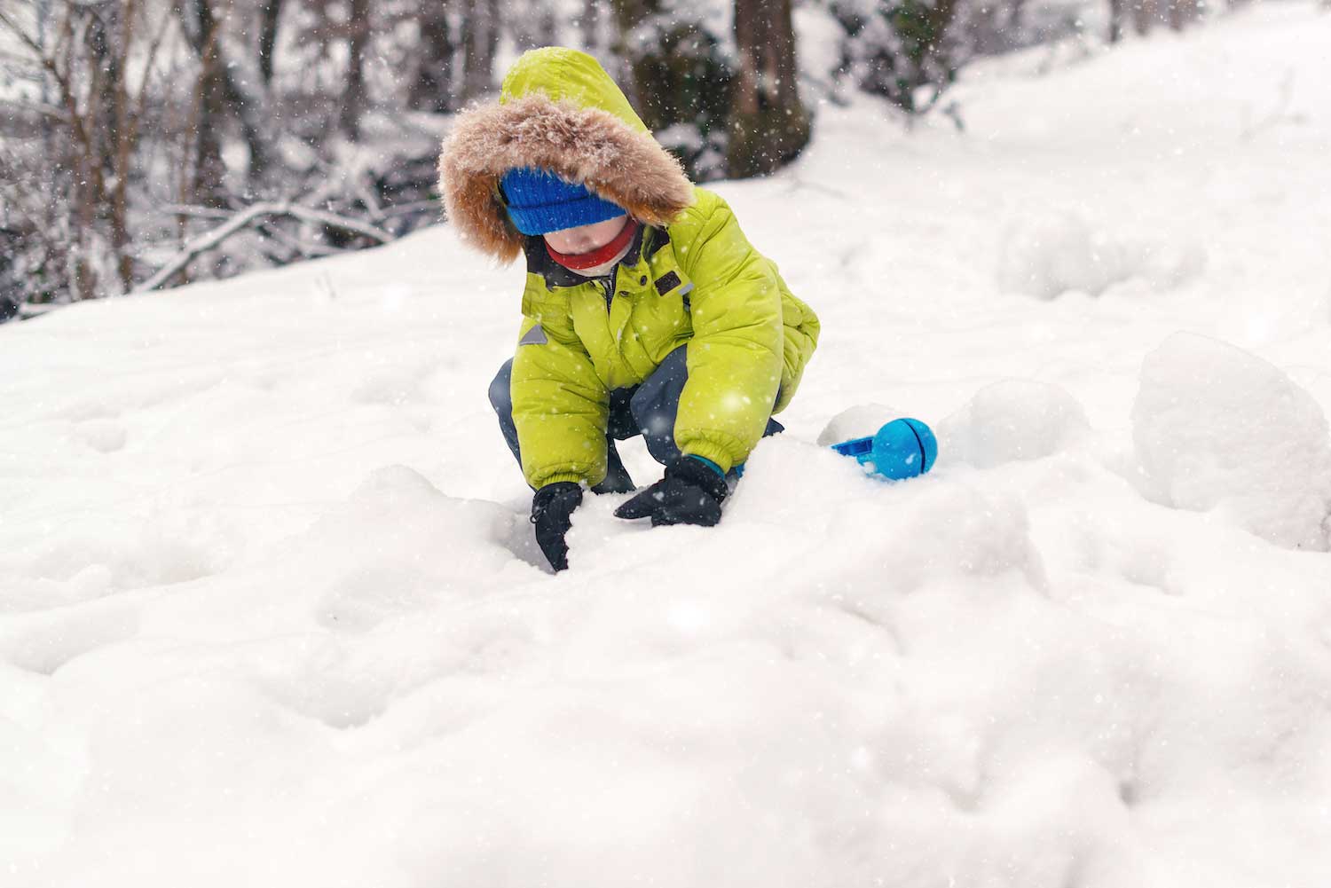 A child playing in the snow while snow is falling.