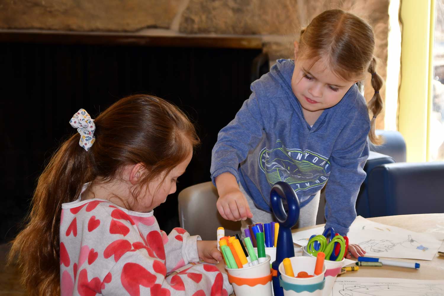 Two children sitting at a table stocked with coloring sheets, crayons, markers and more.