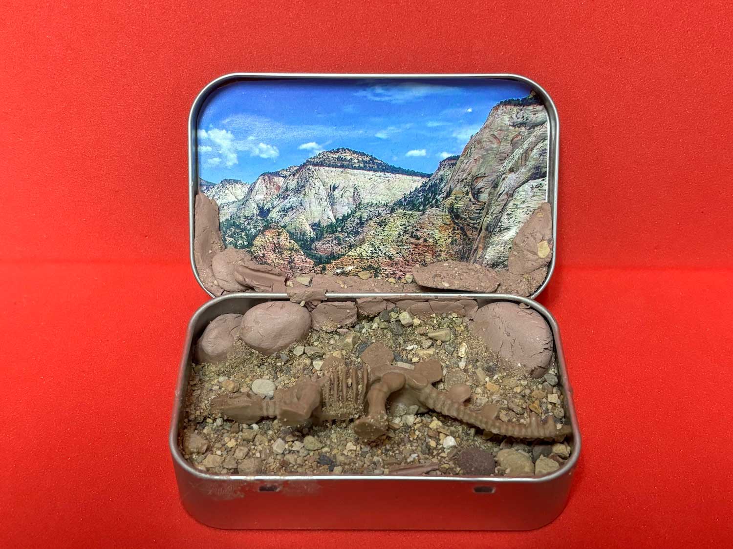 A diorama of a dinosaur habitat created in a small tin.