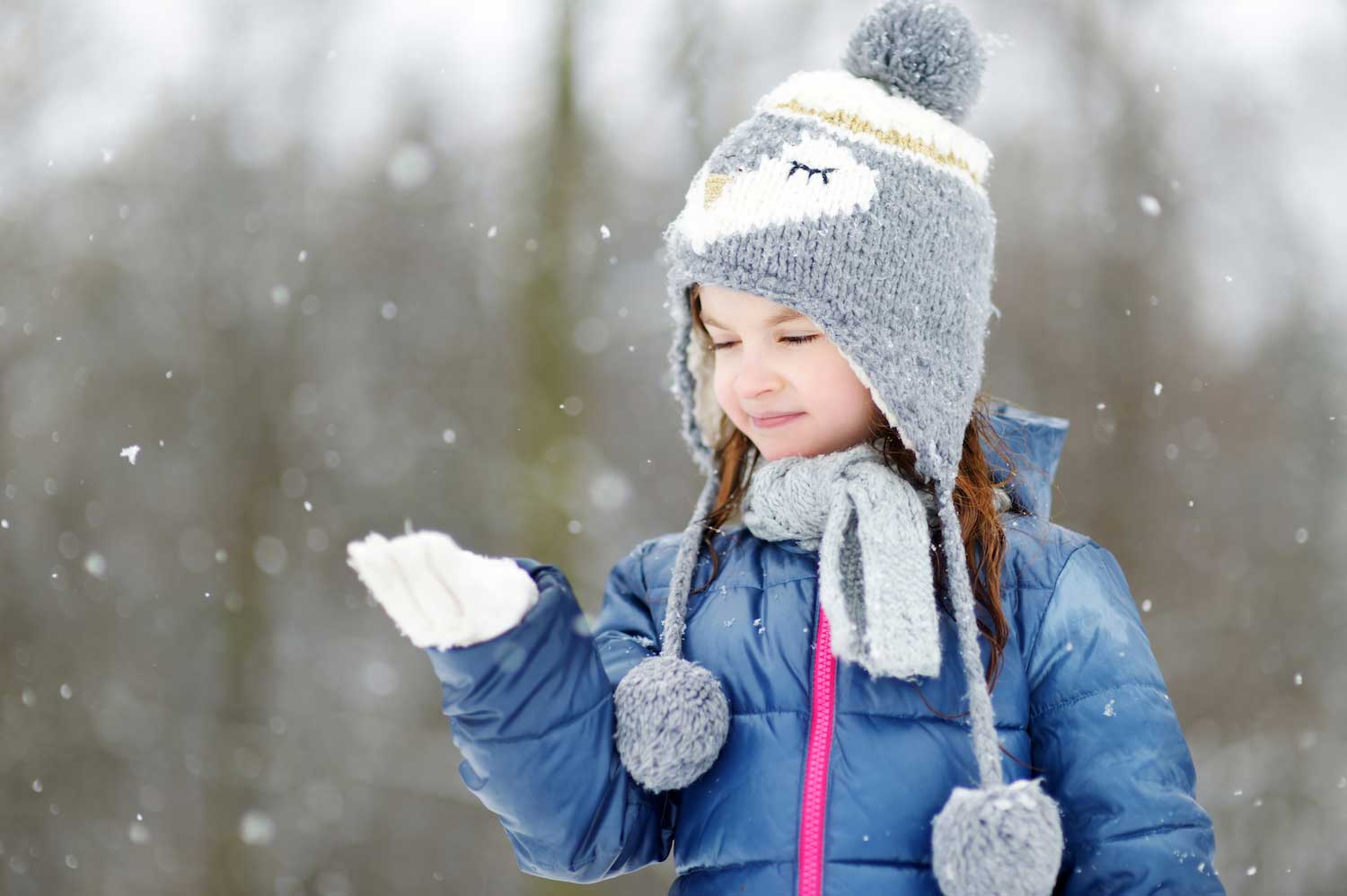 A young child dressed for winter outside in the snow with hand outstretched to catch snowflakes.