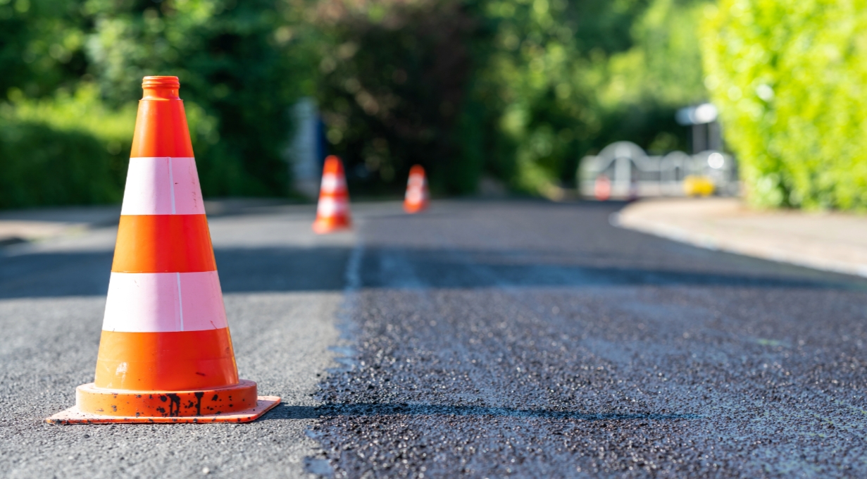 A traffic cone stands beside fresh asphalt.