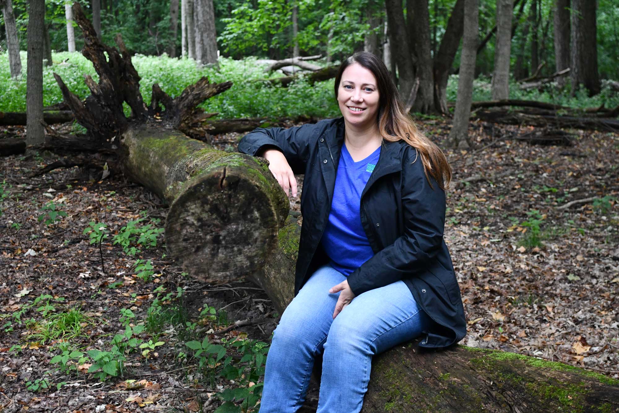 A woman sits on a log in the woods.