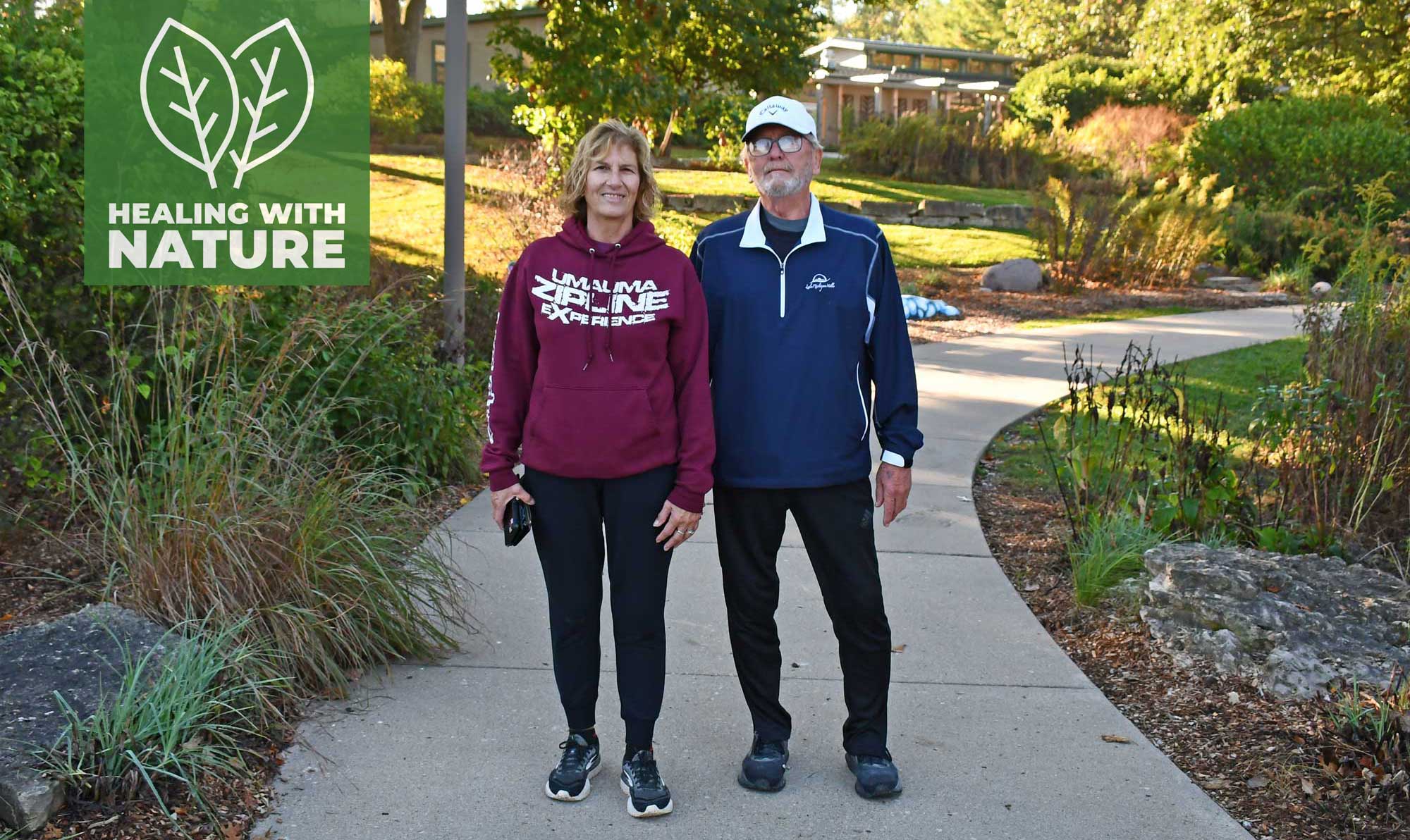 A man and woman stand on a sidewalk in a forest preserve.