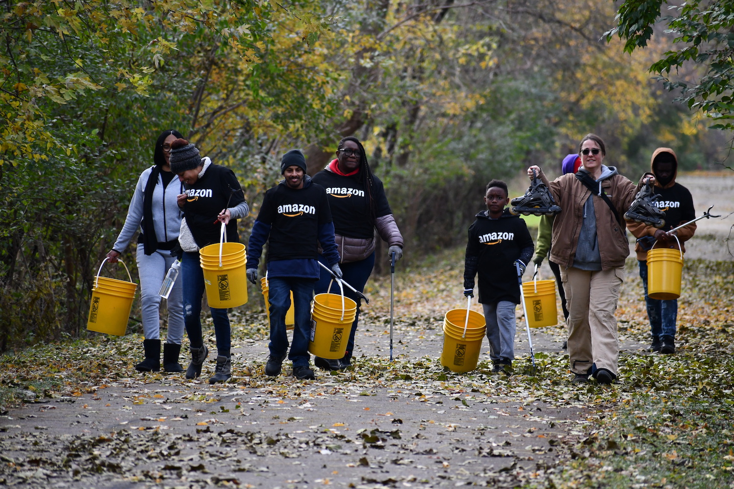 A group of seven people walking along a paved trail holding yellow buckets and grabbers used to pick up litter.