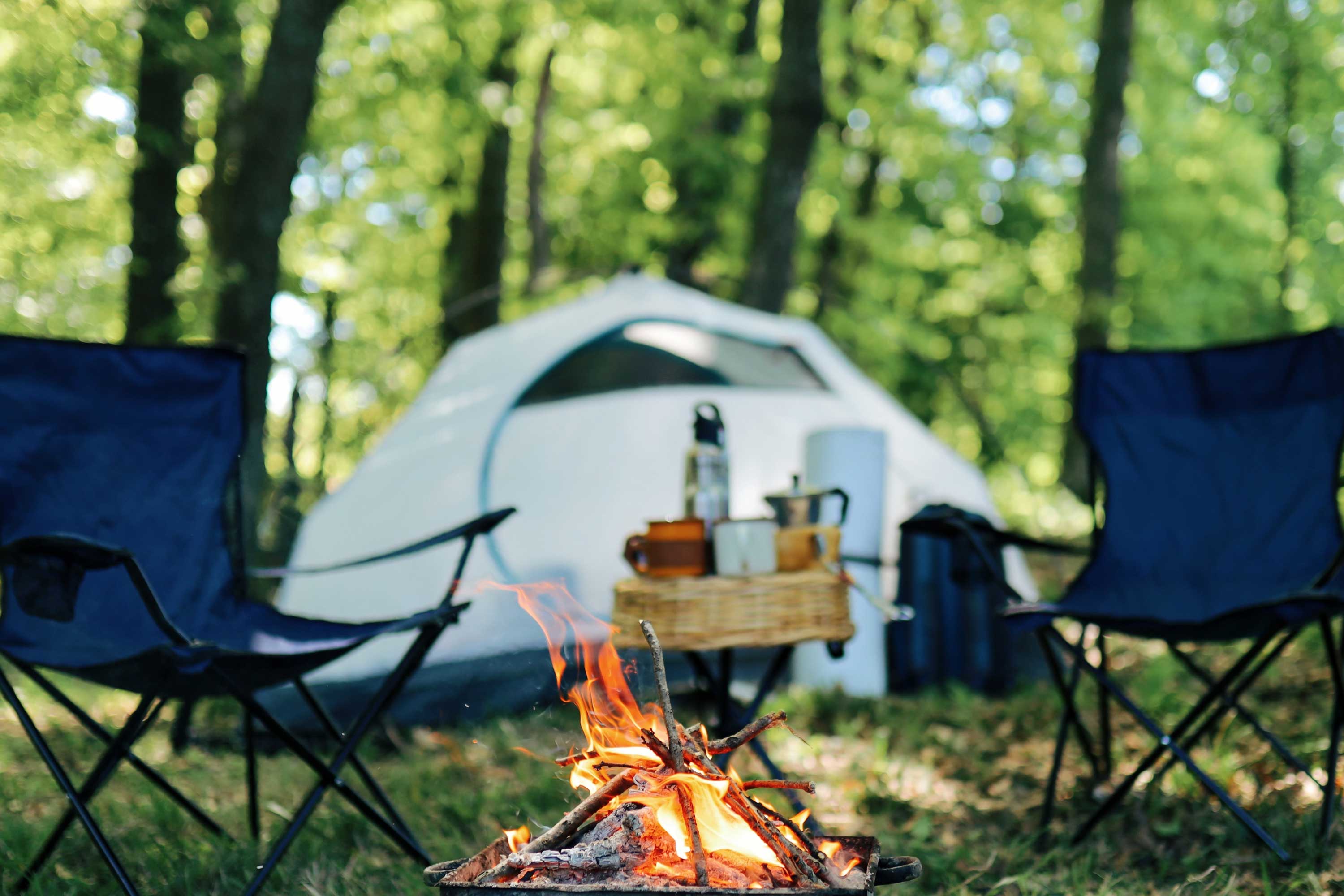 A campsite with a tent, lawn chairs and a fire.