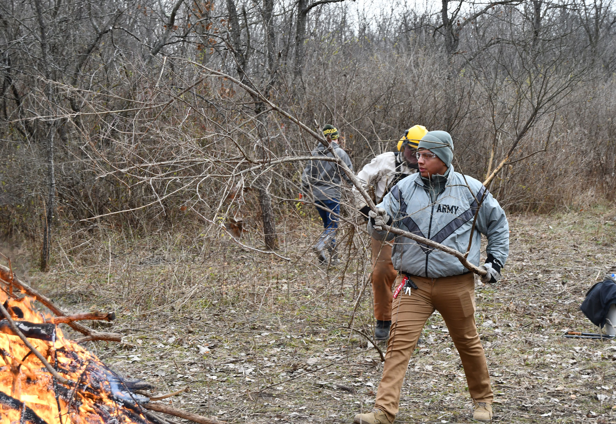 A group of three people holding and carrying brush to a burn pile.