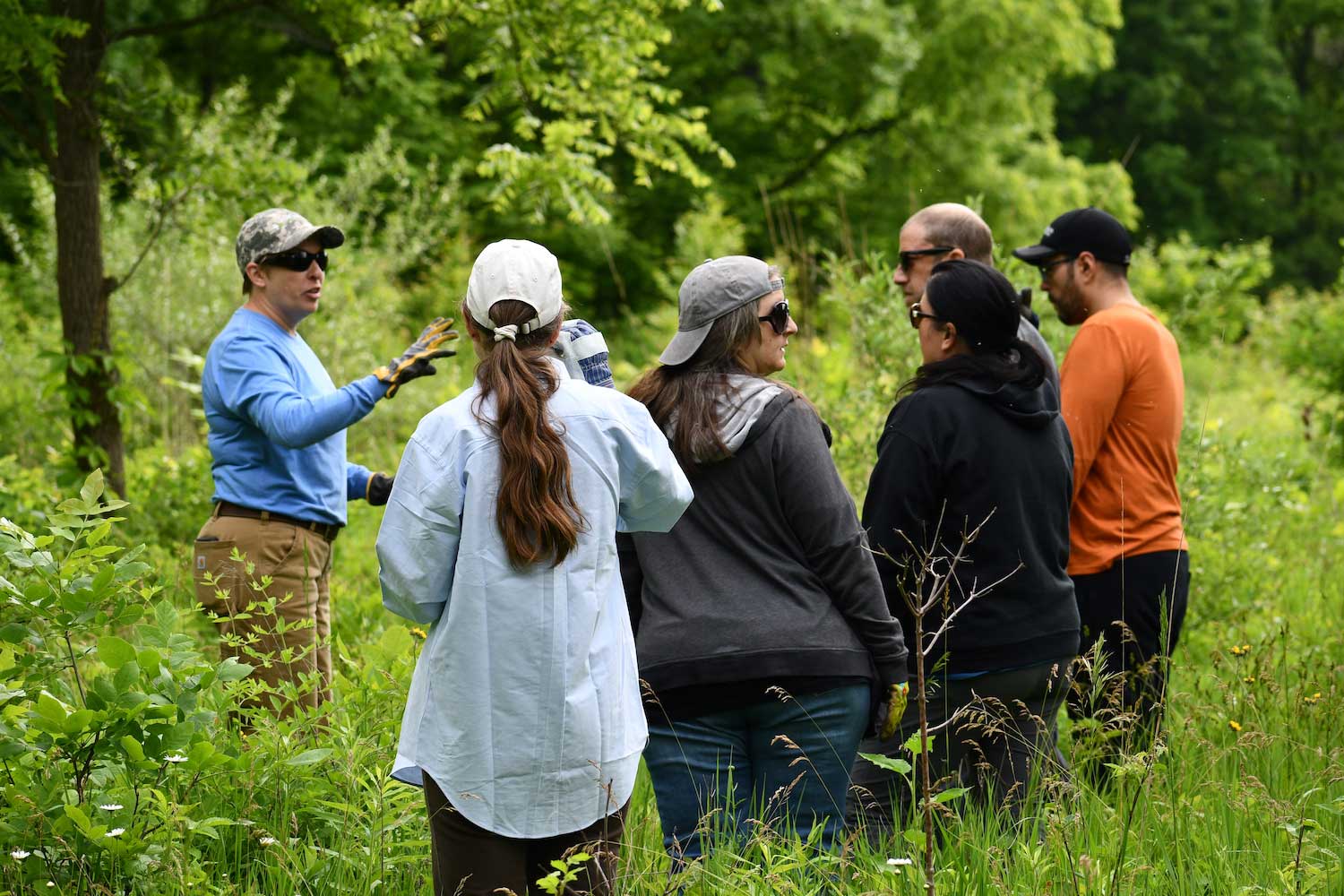 A person standing in a grassy area giving direction to a group of others listening