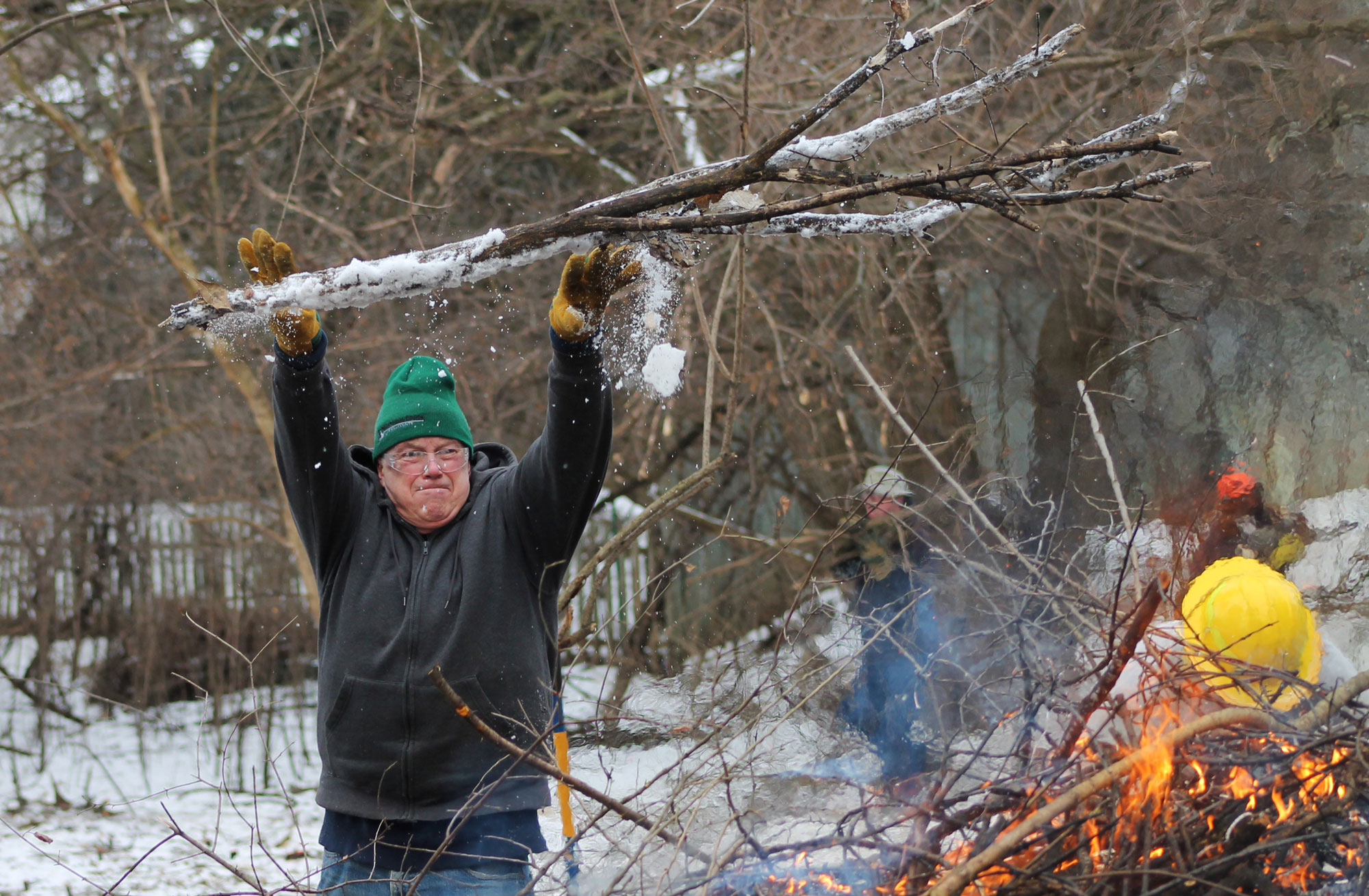 A person hoisting a branch on top of a burning brush pile.