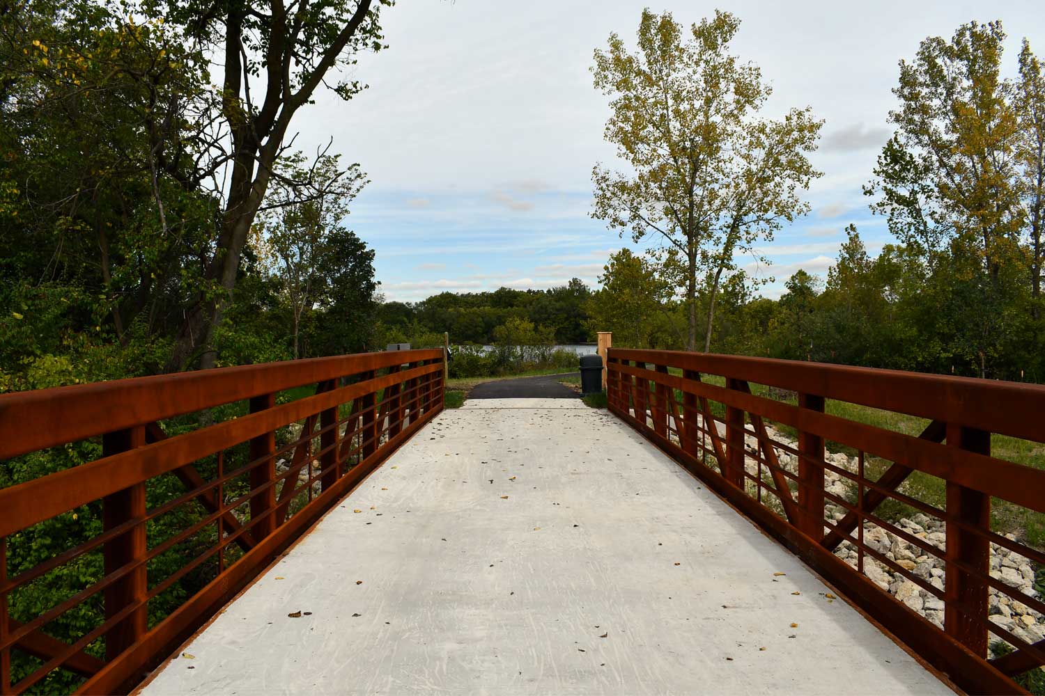 Bridge leading to a paved trail with trees in the background.