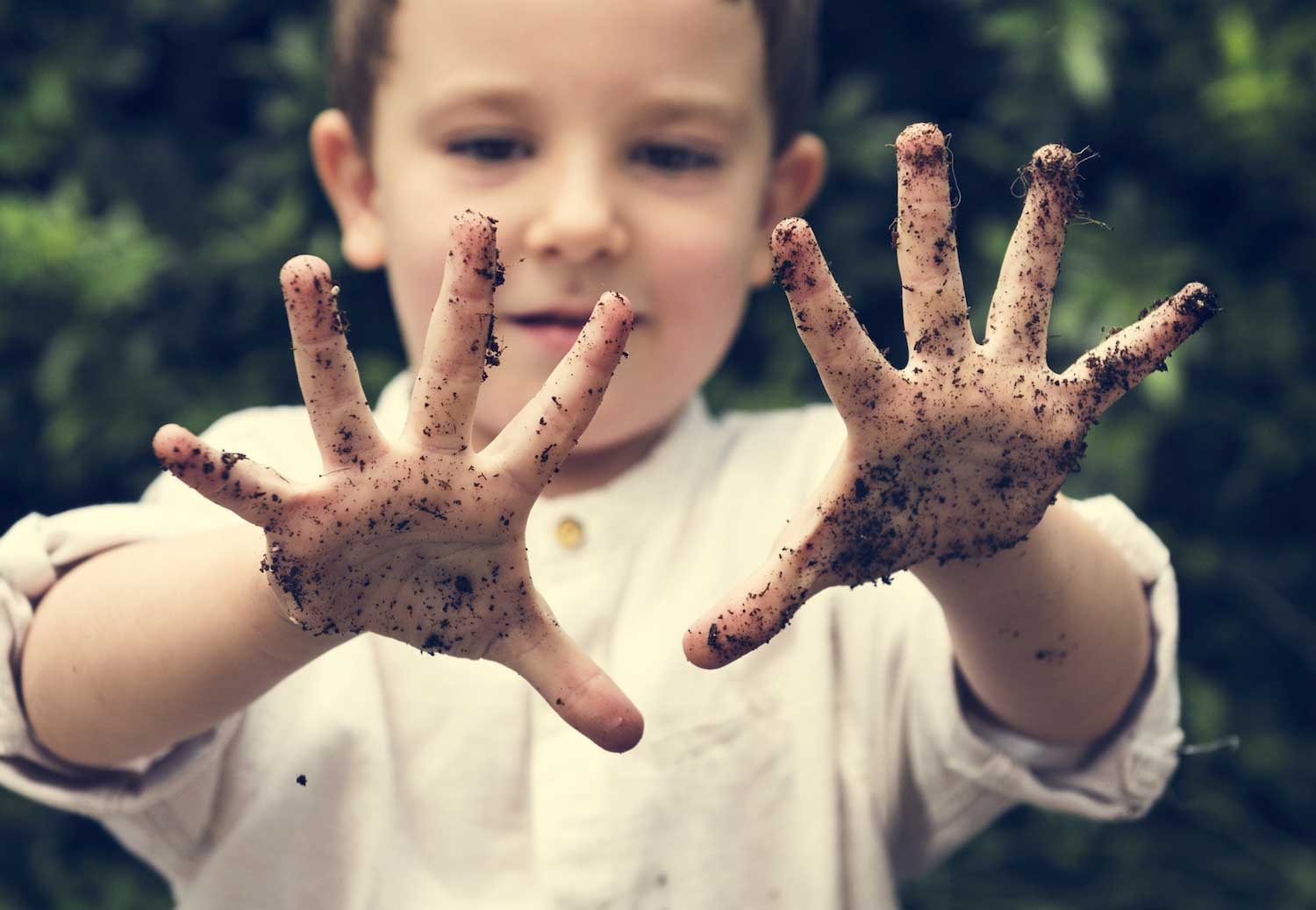 A boy holding out his dirt-covered hands.