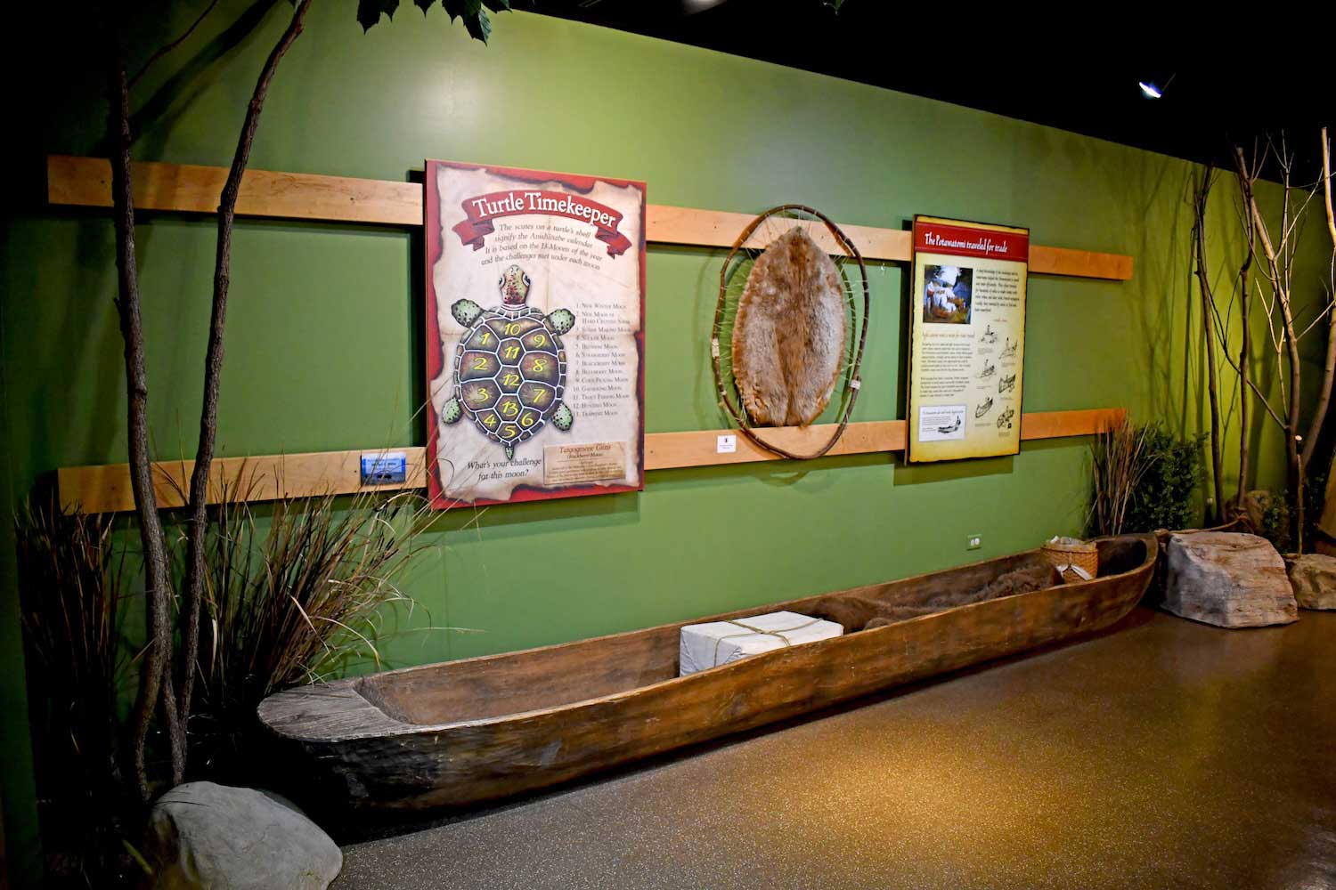 A large wooden canoe on the ground in front of interpretive panels in a museum.