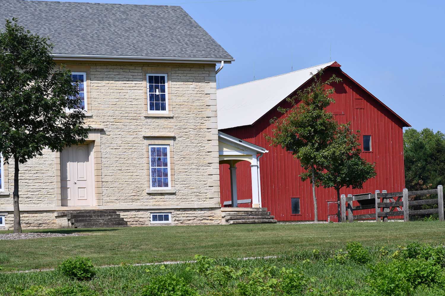 A limestone farmhouse next to a red barn.