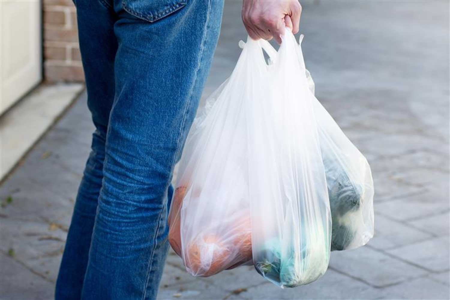 A person walking on a sidewalk carrying plastic shopping bags in their hand.