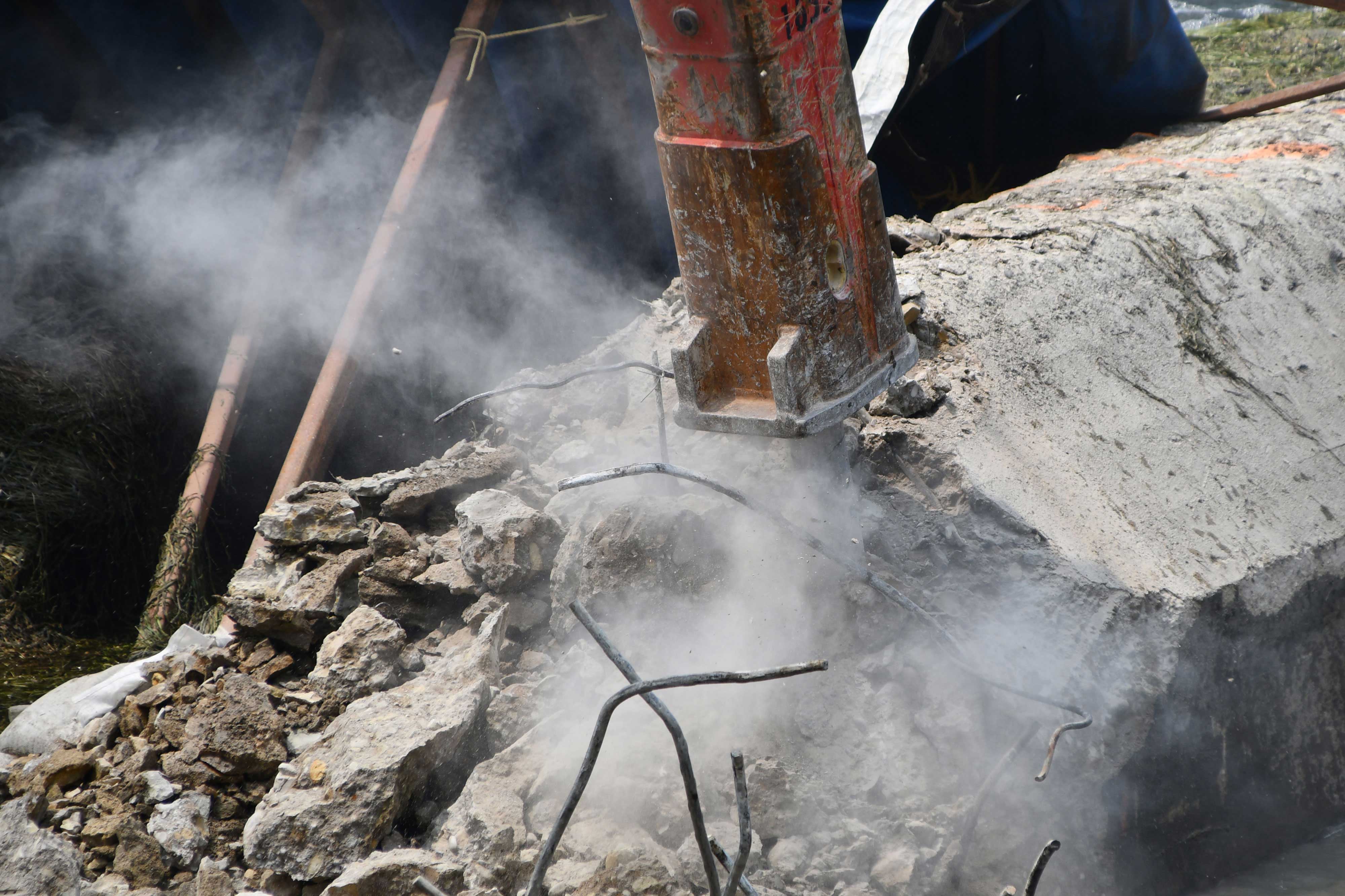 A hydraulic breaker on the end of an excavator chipping away at the dam. 