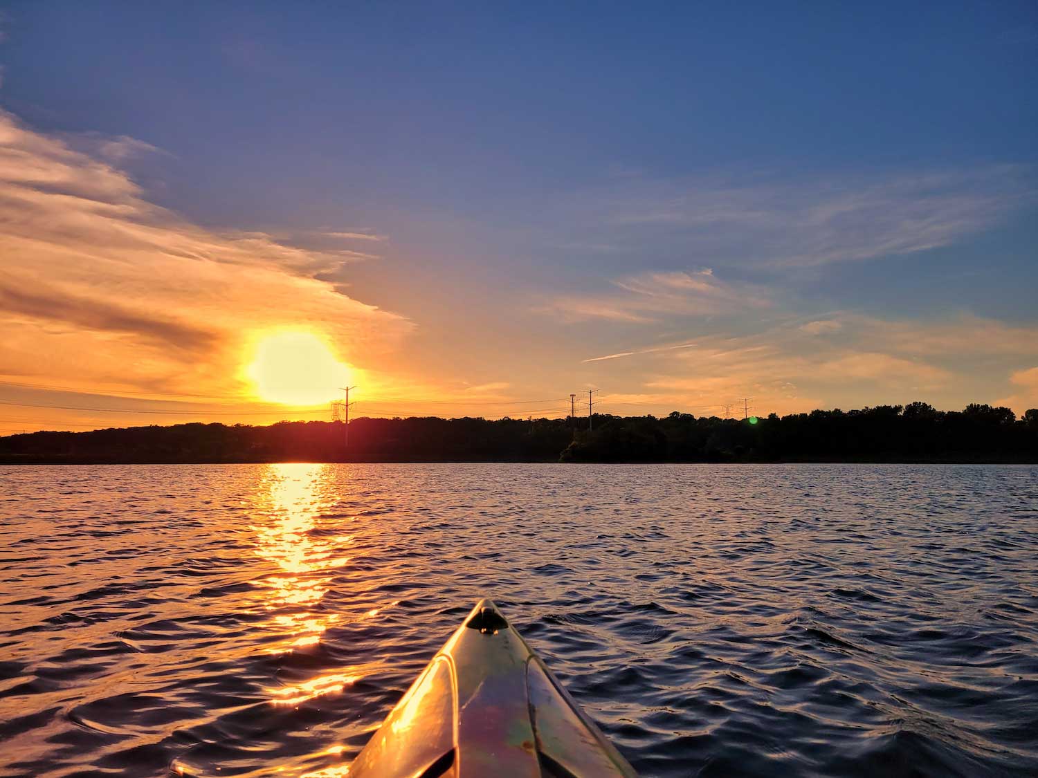 The front of a kayak on open water with a colorful sunset in the background